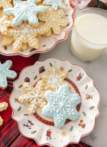 A plate with three differently decorated snowflake cookies by a glass of milk.