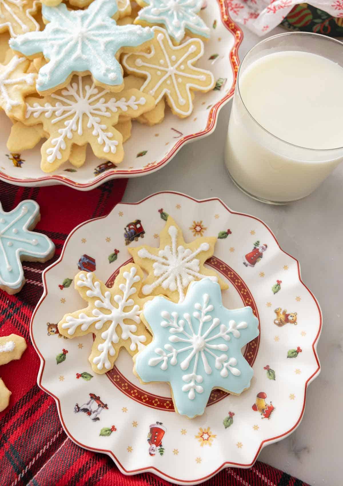 A plate with three differently decorated snowflake cookies by a glass of milk.