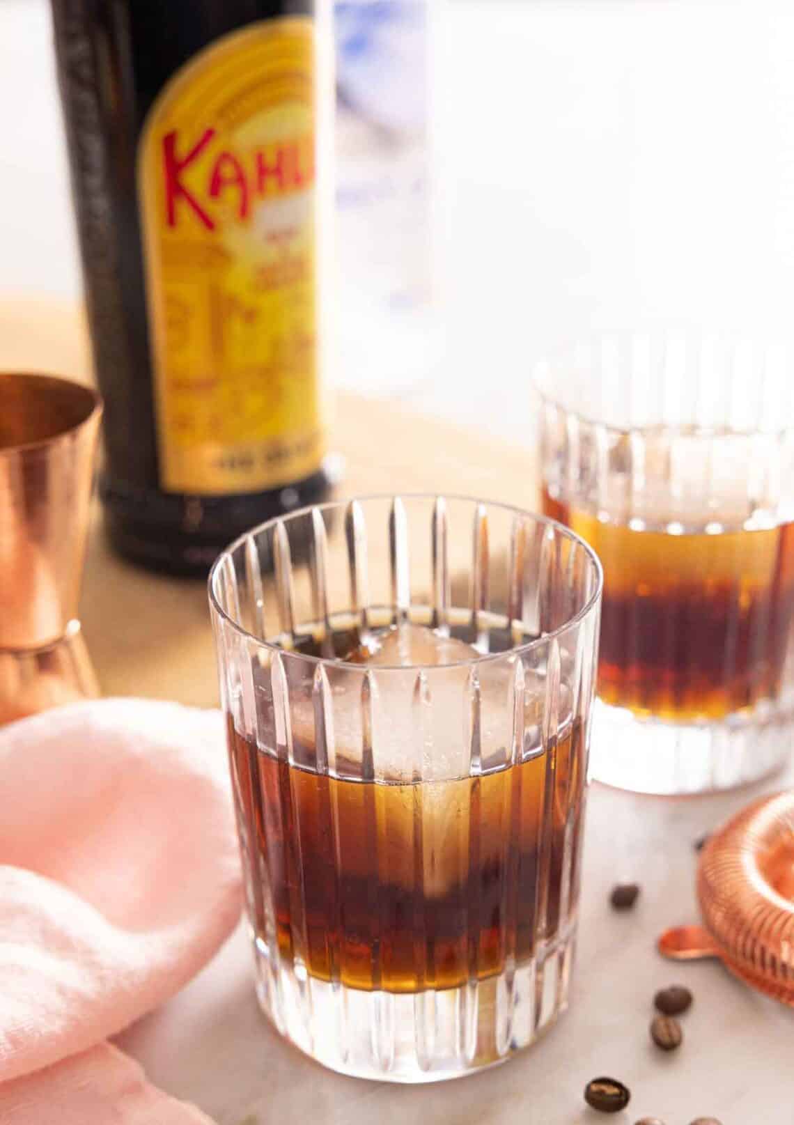 Two glasses of Black Russians with one in front. A bottle of Kahlua in the background.