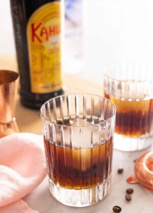 Two glasses of Black Russians with one in front. A bottle of Kahlua in the background.