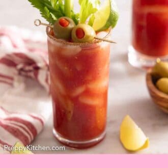 Pinterest graphic of a tall glass of Bloody Mary garnished with olives, lime wedge, and celery.