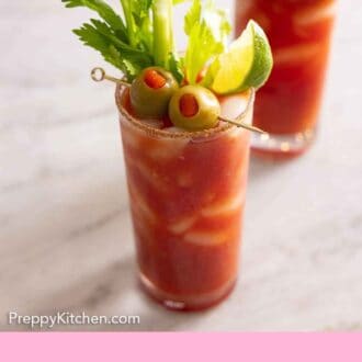 Pinterest graphic of two Bloody Marys, one in front and in focus, with olive, lime, and celery garnish.