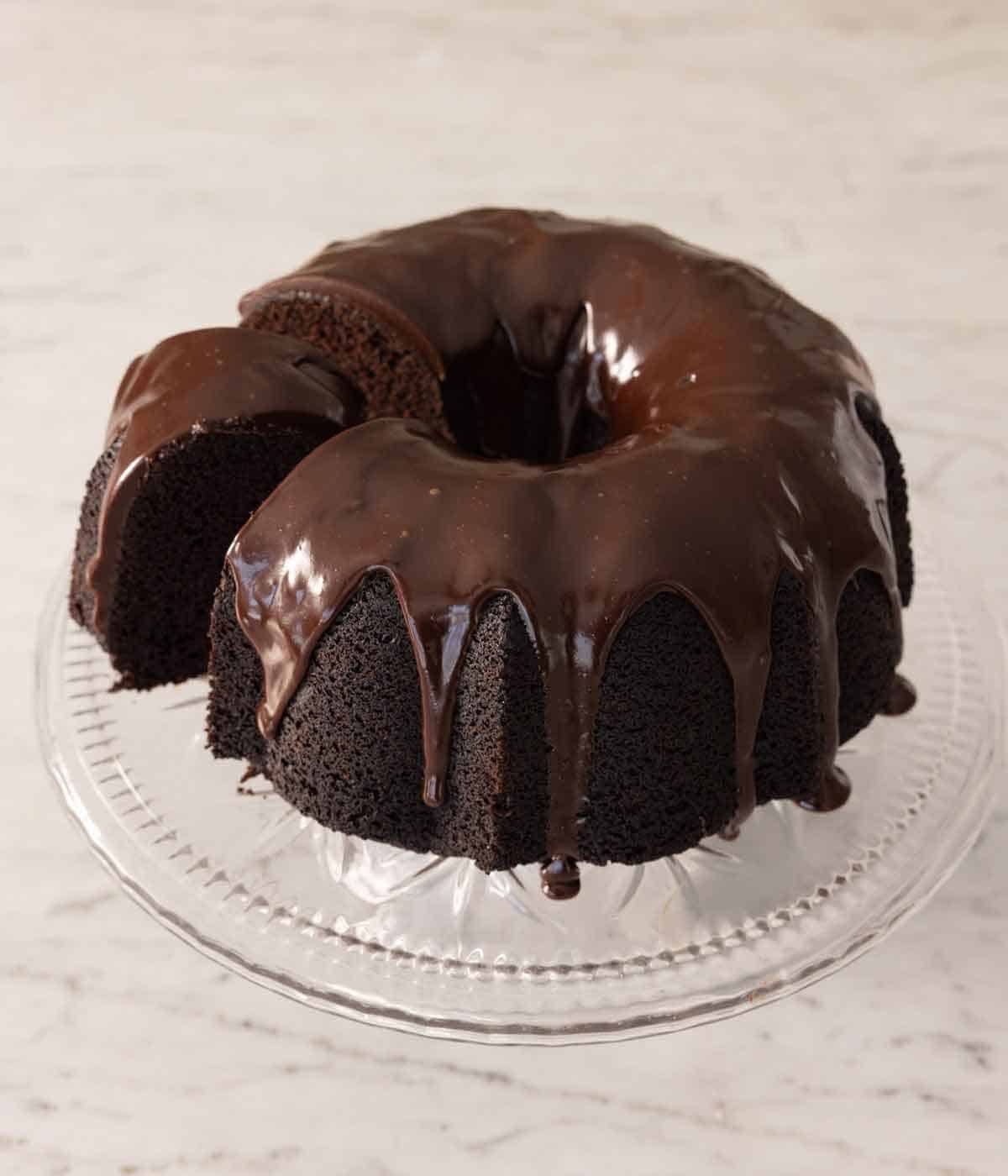A cake stand with chocolate bundt cake with a piece cut and slightly pulled out.