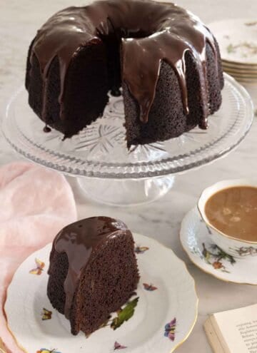A cake stand with a chocolate bundt cake with a slice cut out in front.