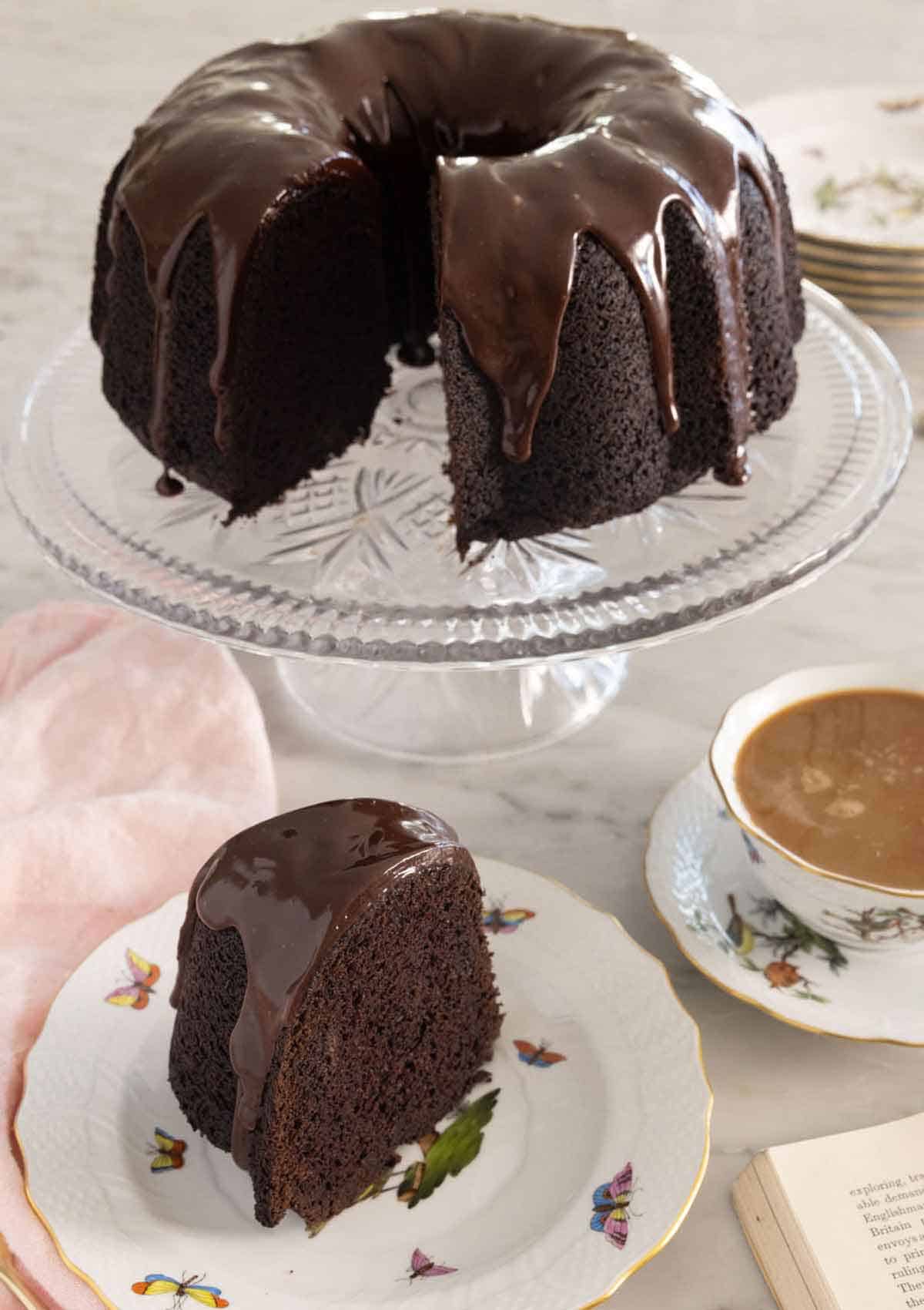 A cake stand with a chocolate bundt cake with a slice cut out in front.