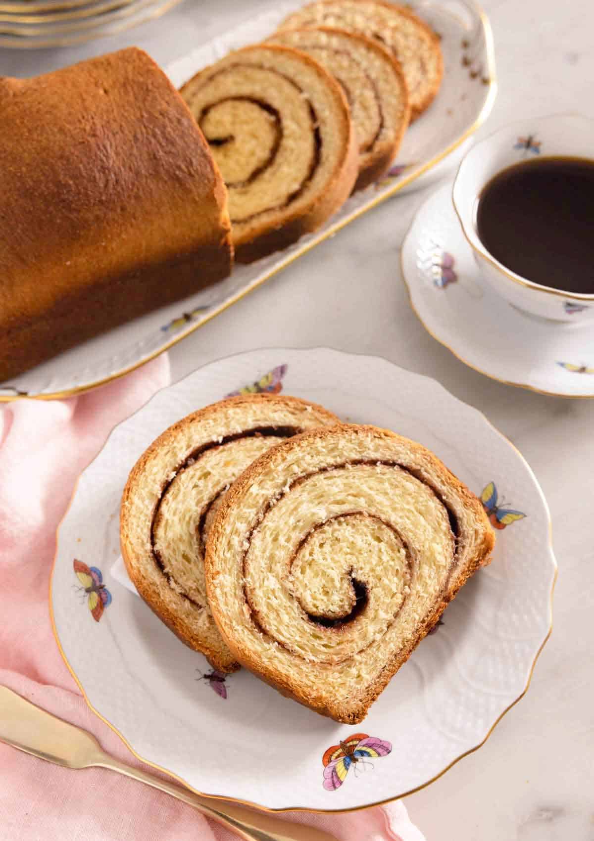 Two slices of cinnamon swirl bread on a plate by a mug of coffee.
