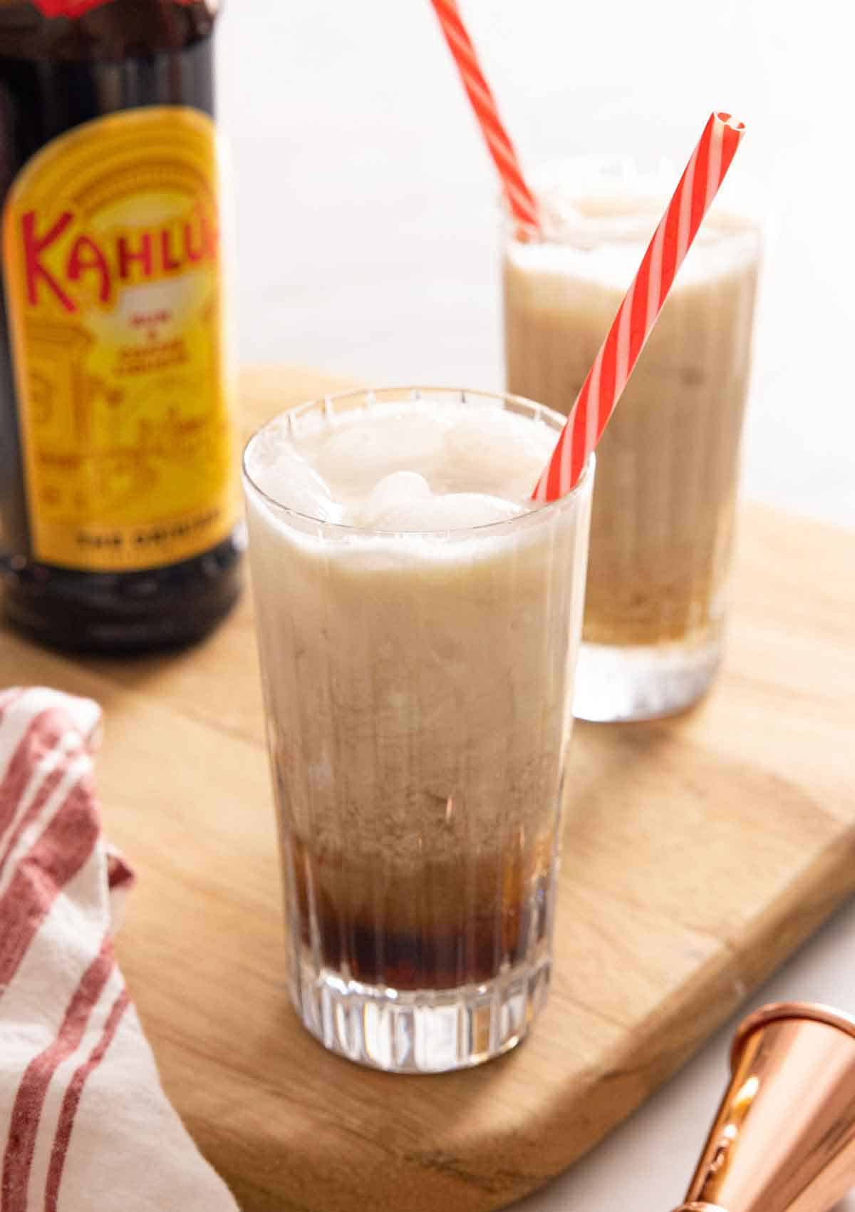 Two glasses of Colorado Bulldog cocktails with a straw with Kahlua in the background.