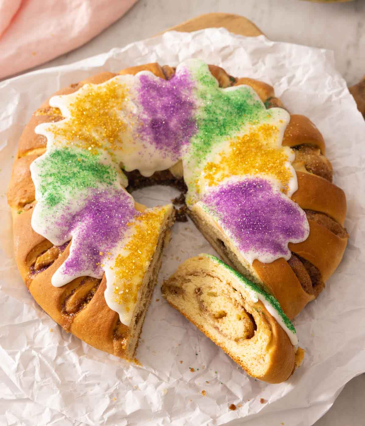 Overhead view of a king cake with purple, green, and yellow sanding sugar with a slice cut.