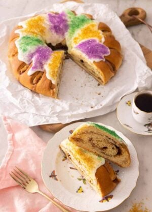 A king cake with two slices cut out, set on a plate in front of it.