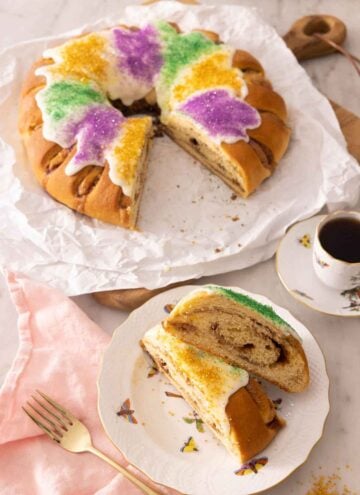 A king cake with two slices cut out, set on a plate in front of it.