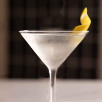 A profile view of a glass of martini with a lemon twist.