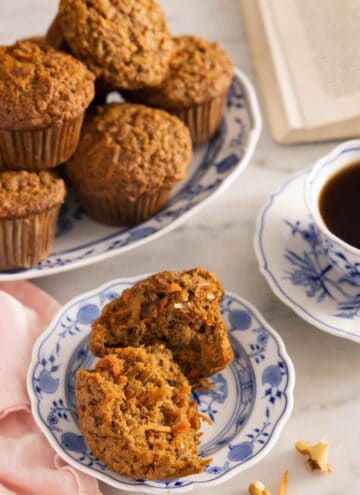 A plate with a morning glory muffins cut in half in front of a platter of muffins.