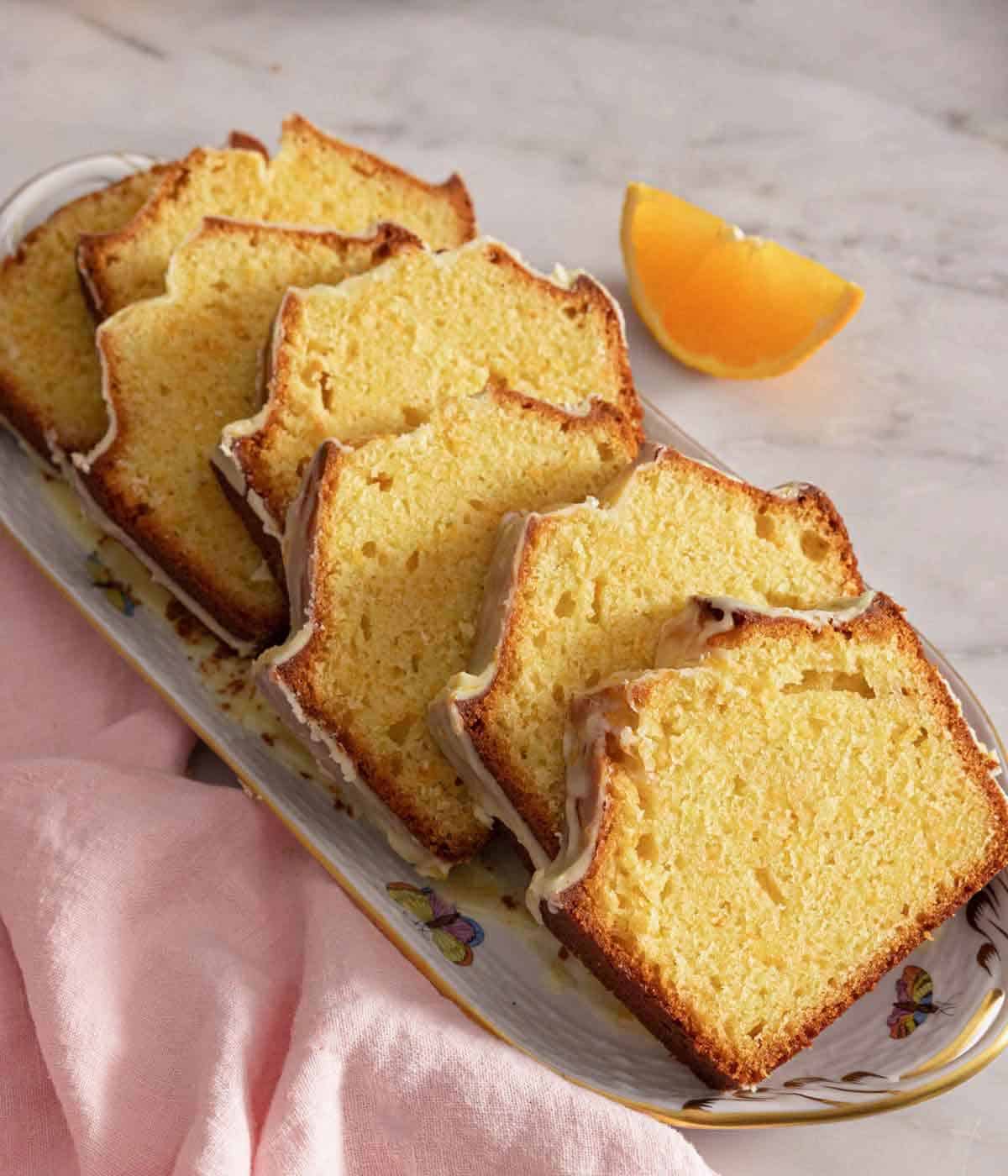 A long plate with slices of orange cake with a fresh orange wedge beside it.