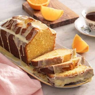 A platter of orange cake with slices cut in front by a mug of coffee.
