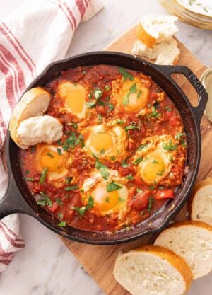 Overhead view of a cast-iron of shakshuka with bread dipped in and around the pan.