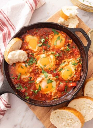Overhead view of a cast-iron of shakshuka with bread dipped in and around the pan.