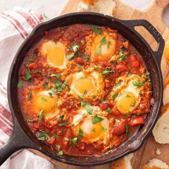 A cast iron with shakshuka with sliced bread beside it on a serving board.