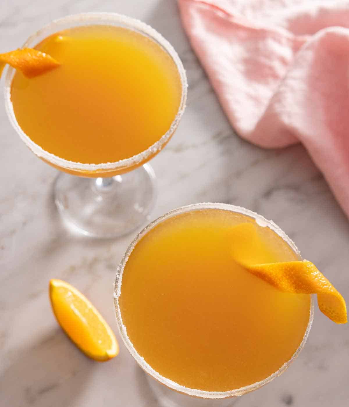 Overhead view of two glasses of sidecar cocktails with an orange twist.