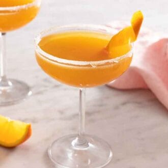 Two glasses of sidecar cocktails with an orange wedge and linen beside it.