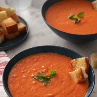 Pinterest graphic of two bowls of tomato soup with basil and croutons on top.
