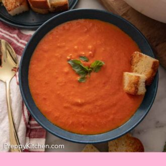Pinterest graphic of a bowl of tomato soup with some basil and croutons.