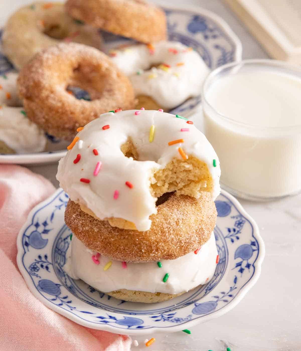 A stack of three baked donuts by a glass of milk.