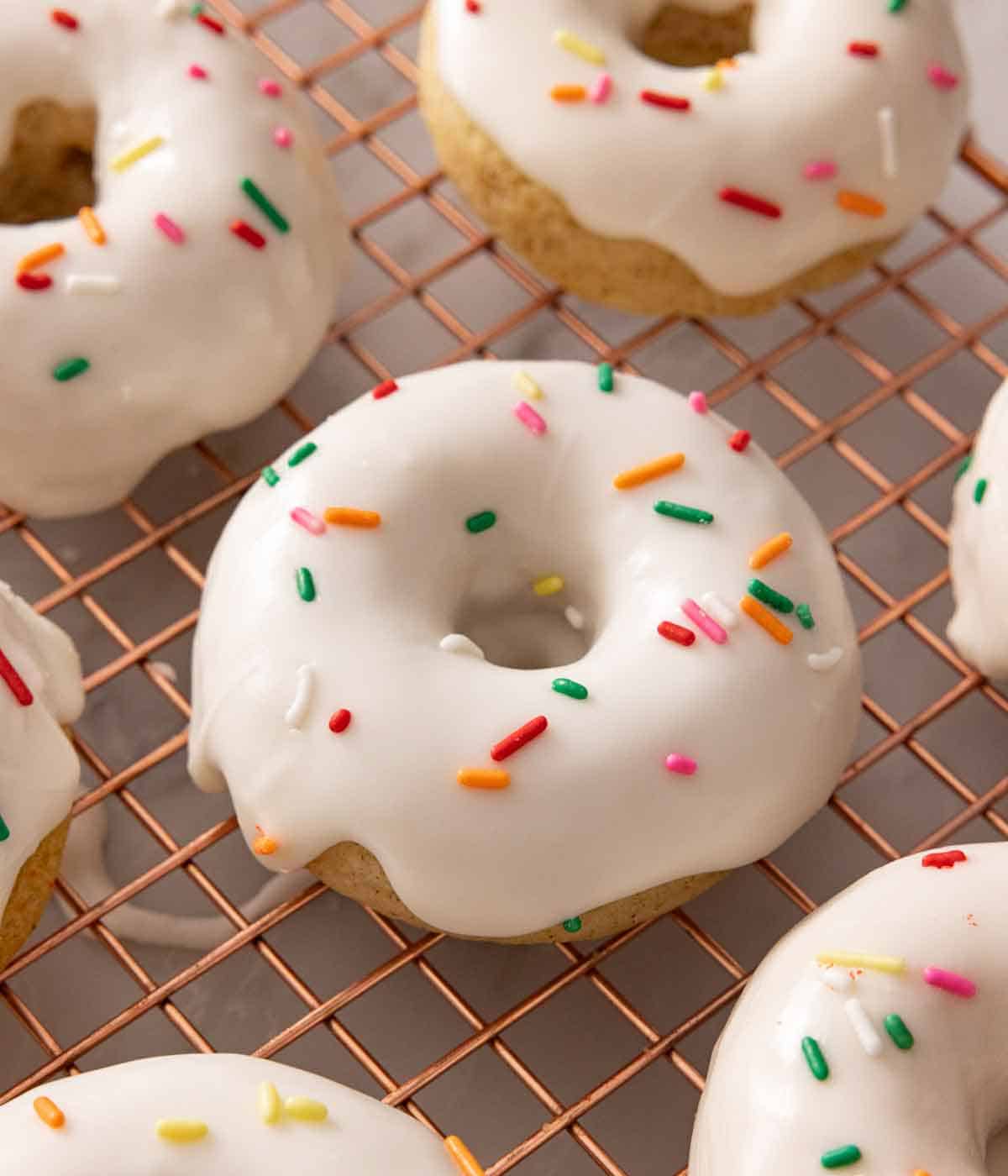 Multiple glazed and sprinkled baked donuts on a wire rack.