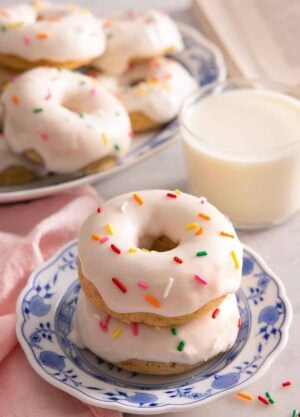 A plate with two stacked baked donuts with glaze and sprinkles on top.