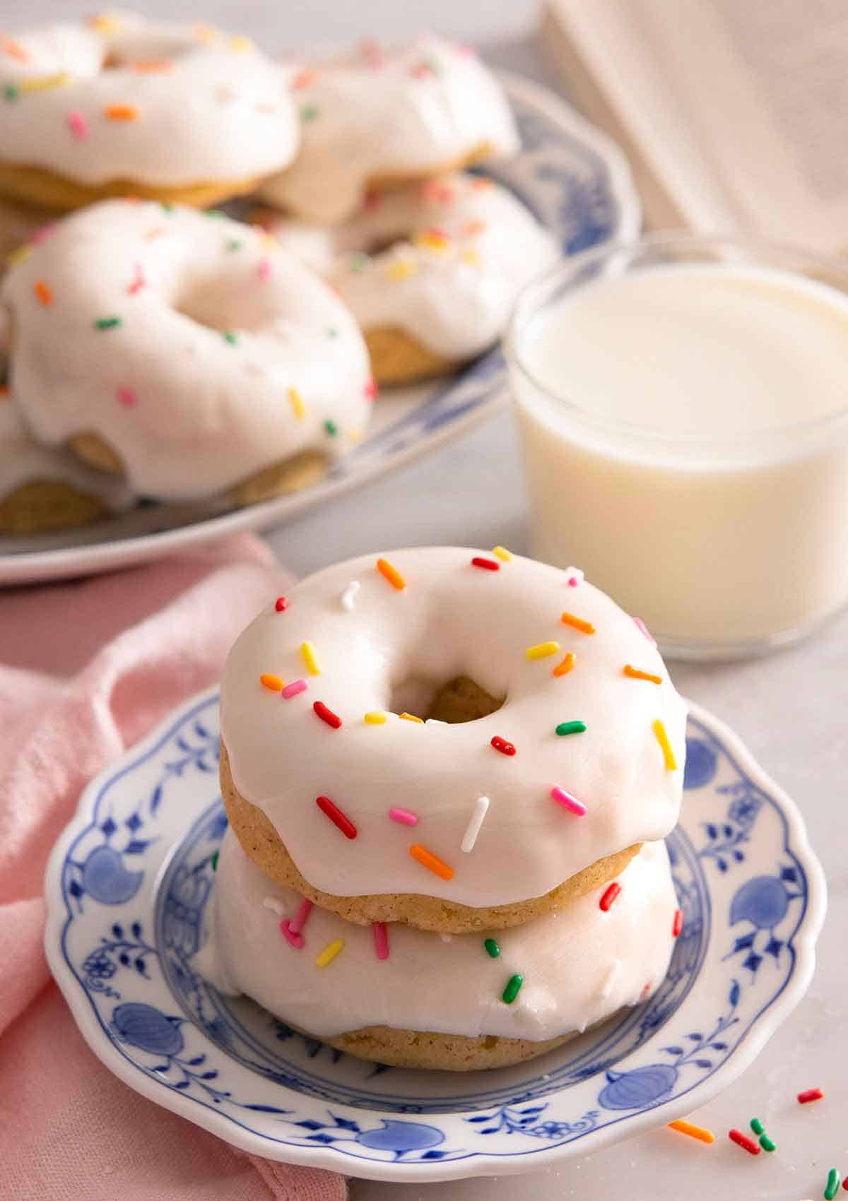 A plate with two stacked baked donuts with glaze and sprinkles on top.