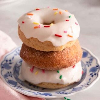 A stack of three baked donuts, two with glaze and sprinkles on a plate.