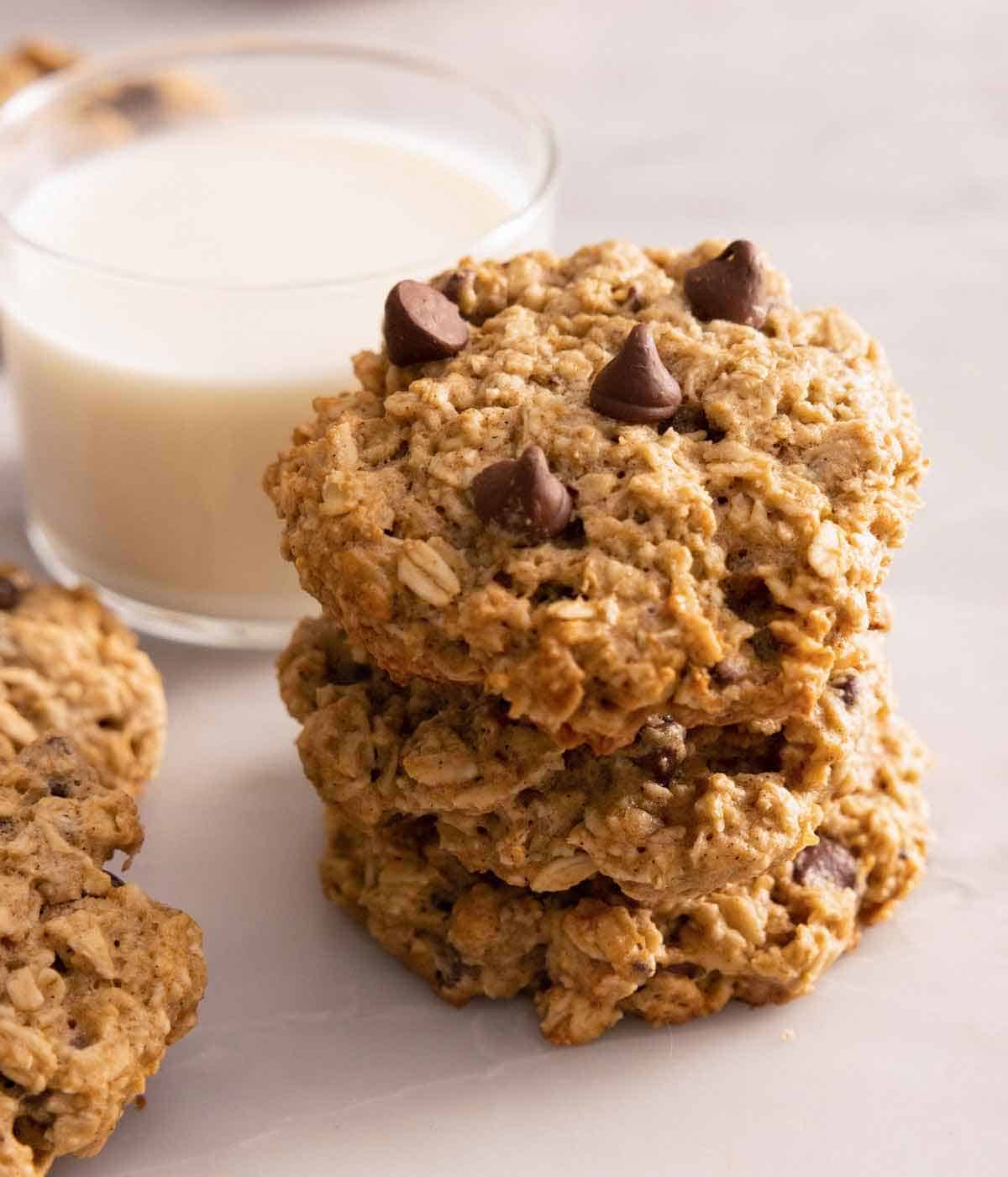 A stack of three banana oatmeal cookies by a glass of milk.