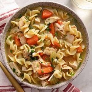 A bowl of chicken noodle soup with a spoon beside it.