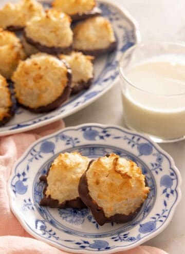 A plate with two coconut macaroons in front of a glass of milk and a platter.
