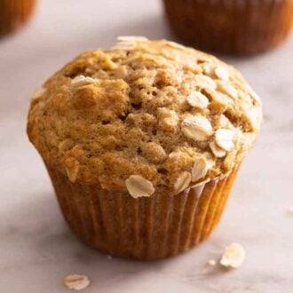 An oatmeal muffin with pieces of oats scattered around it.