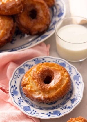 A plate with an old fashioned donut in front of a glass of milk.