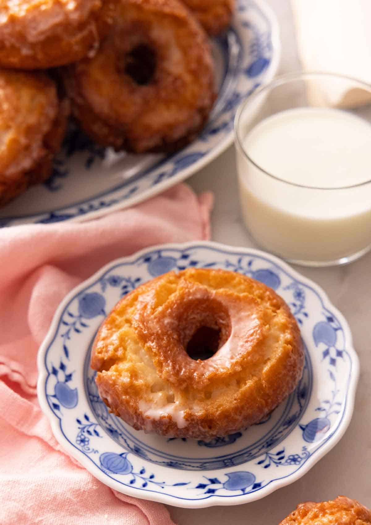 A plate with an old fashioned donut in front of a glass of milk.
