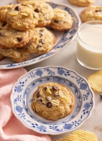 A potato chip cookie on a plate by a glass of milk and more cookies.
