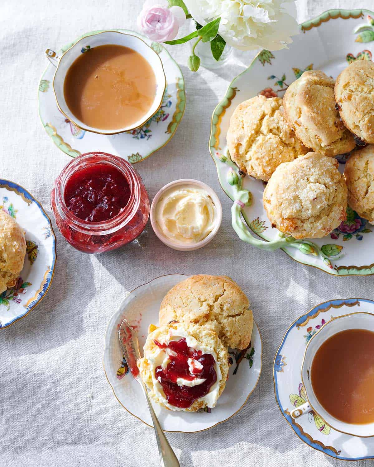 An overhead shot of scones with clotted cream and jam next to cups of tea. 