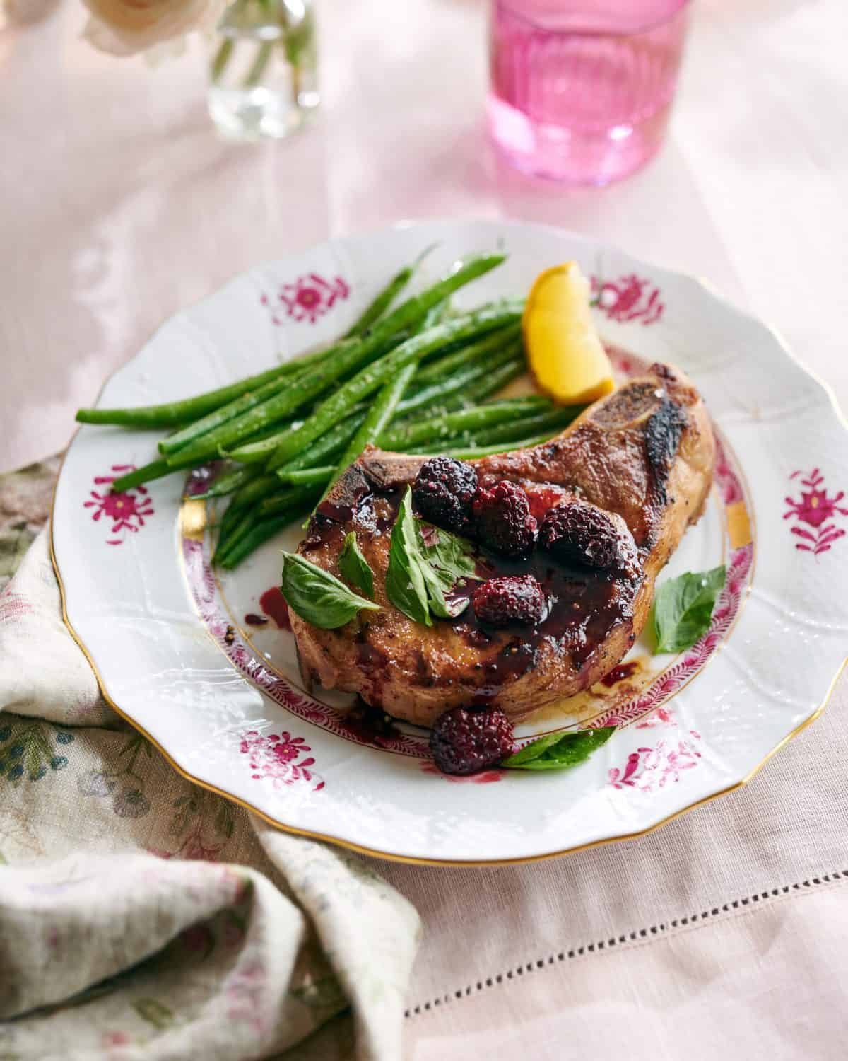 A pork chop covered in roasted blackberries next to green beans.