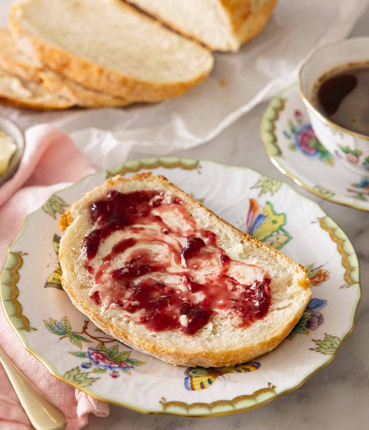 A plate with a slice of artisan bread with butter and jam spread over.