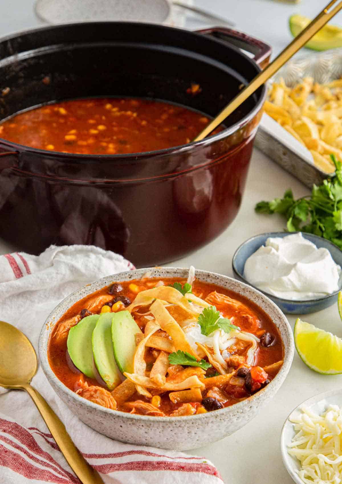 A bowl of chicken tortilla soup in front of a dutch oven with more soup.