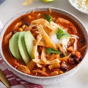 A bowl of chicken tortilla soup with avocado and cilantro on top.