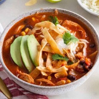 A bowl of chicken tortilla soup with avocado and cilantro on top.