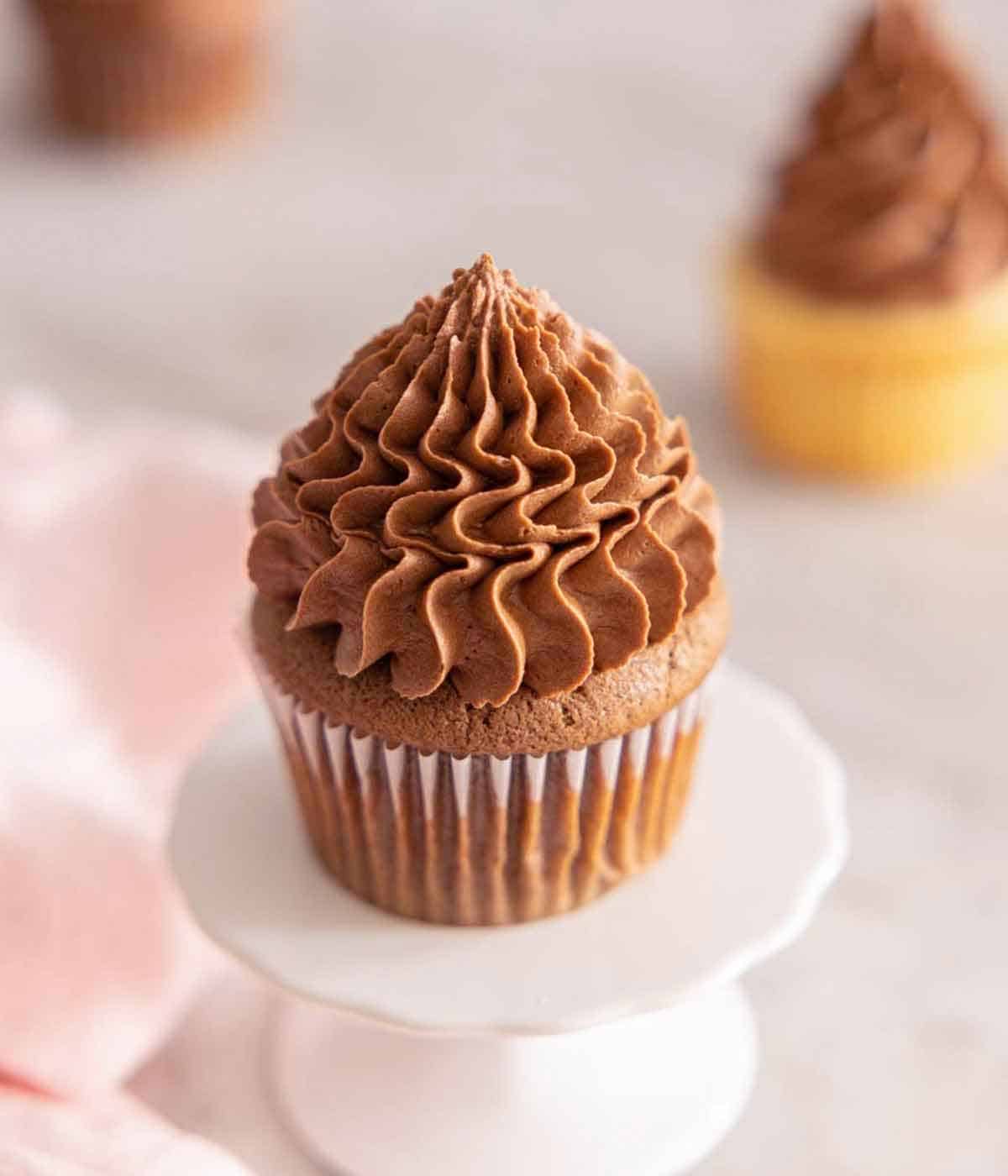 A cupcake with chocolate buttercream frosting on top, on a mini cake stand.