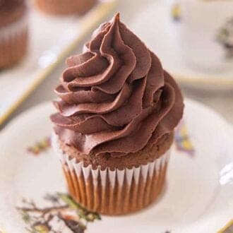 A plate with a cupcake with chocolate buttercream frosting on top.