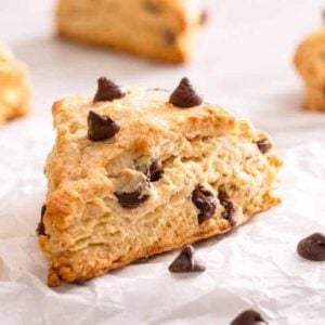 Multiple chocolate chip scones on a sheet of parchment with one in focus.