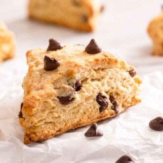 Multiple chocolate chip scones on a sheet of parchment with one in focus.