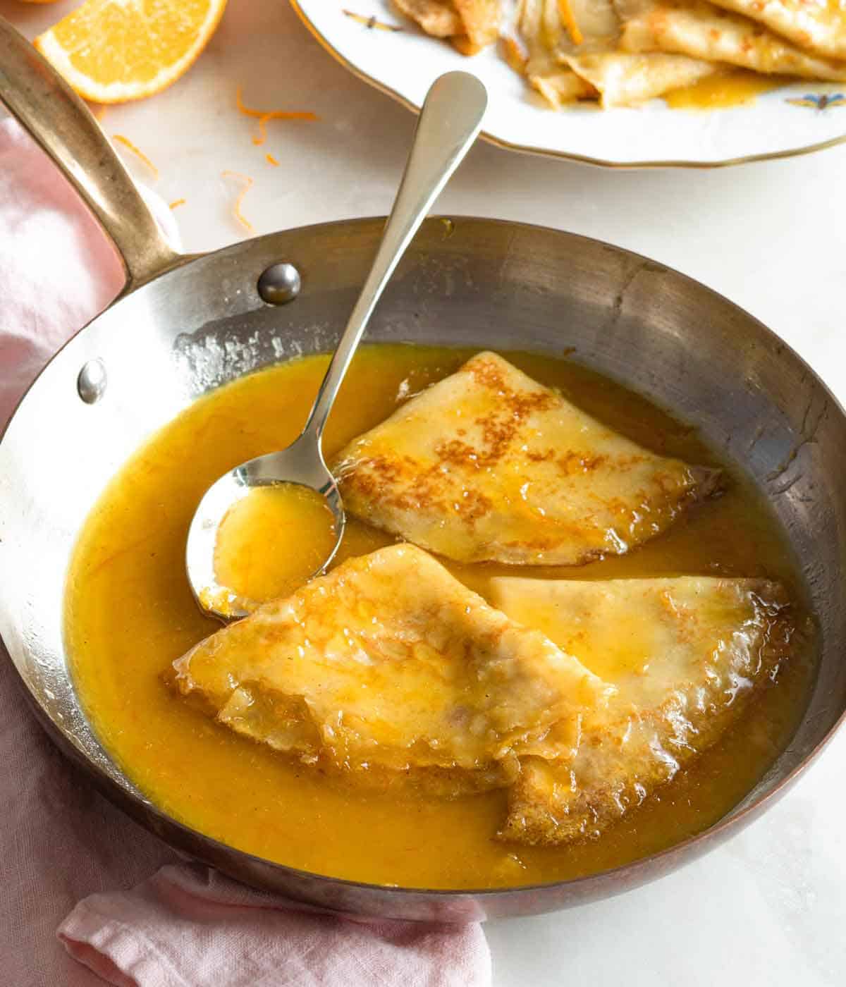 A skillet with three crepe suzette with a spoon filled with sauce.