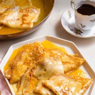Pinterest graphic of a plate with a few crepe suzette by a cup of coffee and a pan of more crepes.