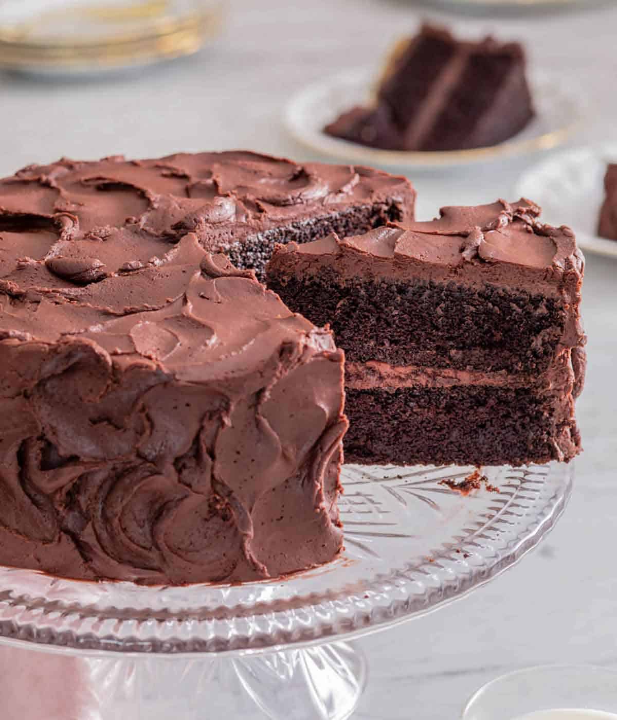 A cake stand with a devil’s food cake with a slice cut and slightly pulled out.